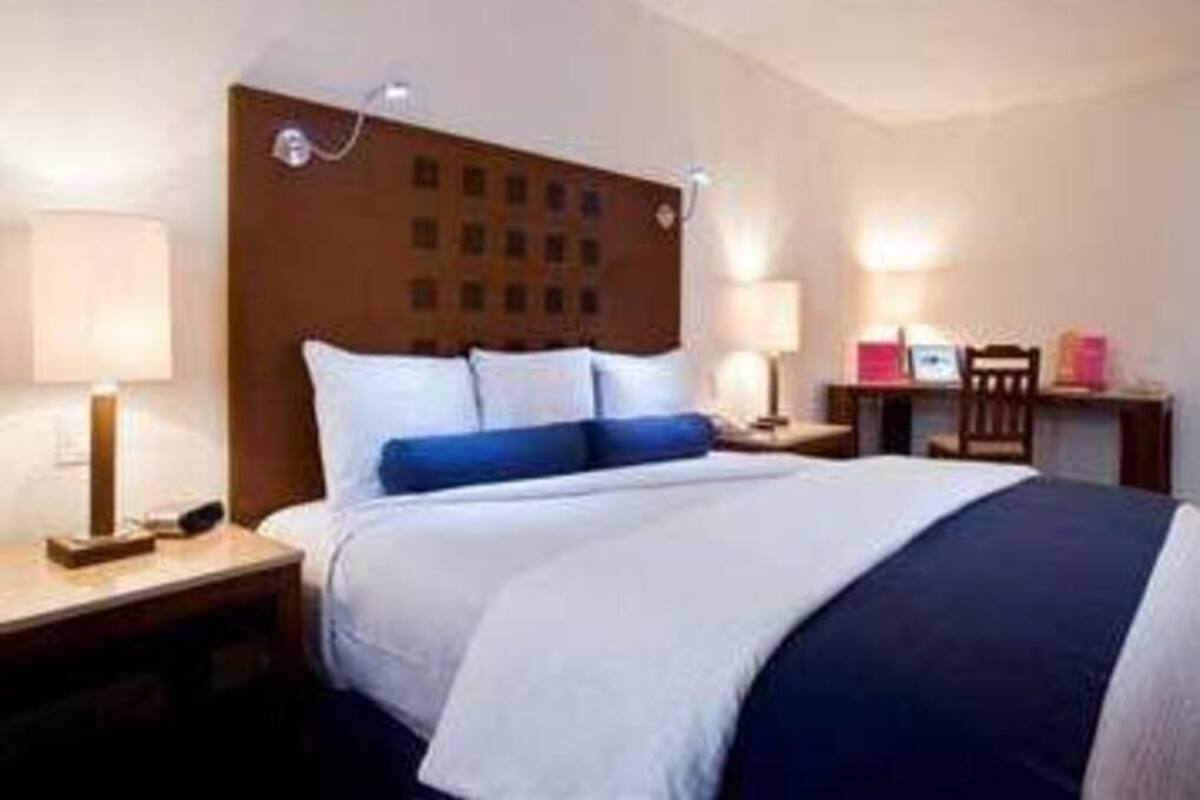 A hotel room with a bed, bedside lamps, a nightstand, and a desk with a chair.