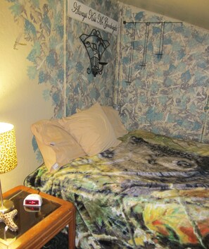 A bedroom with a bed, a nightstand, a lamp, and a wall tapestry. - Downtown Craig (Craig)
