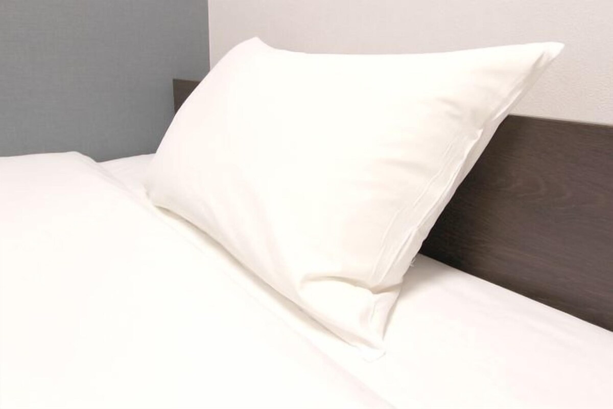 Una cama bien tendida con un almohadón blanco y un cabecero oscuro.