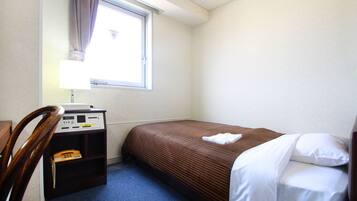 Une petite chambre d’hôtel avec un lit simple, un bureau avec un téléphone et une fenêtre avec des rideaux.