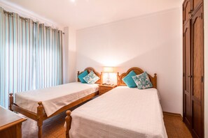Une chambre avec deux lits simples, des têtes de lit en bois, une table de chevet avec une lampe et une armoire.