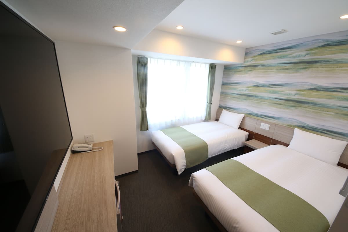 A hotel room with two beds, a desk with a telephone, and a large abstract painting on the wall.