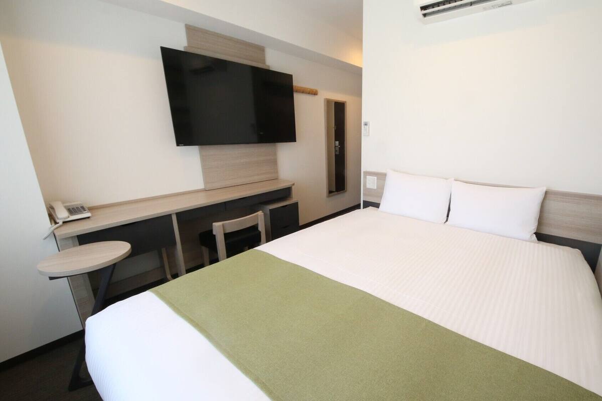 A hotel room with a bed, a desk, a chair, a television, and a telephone.