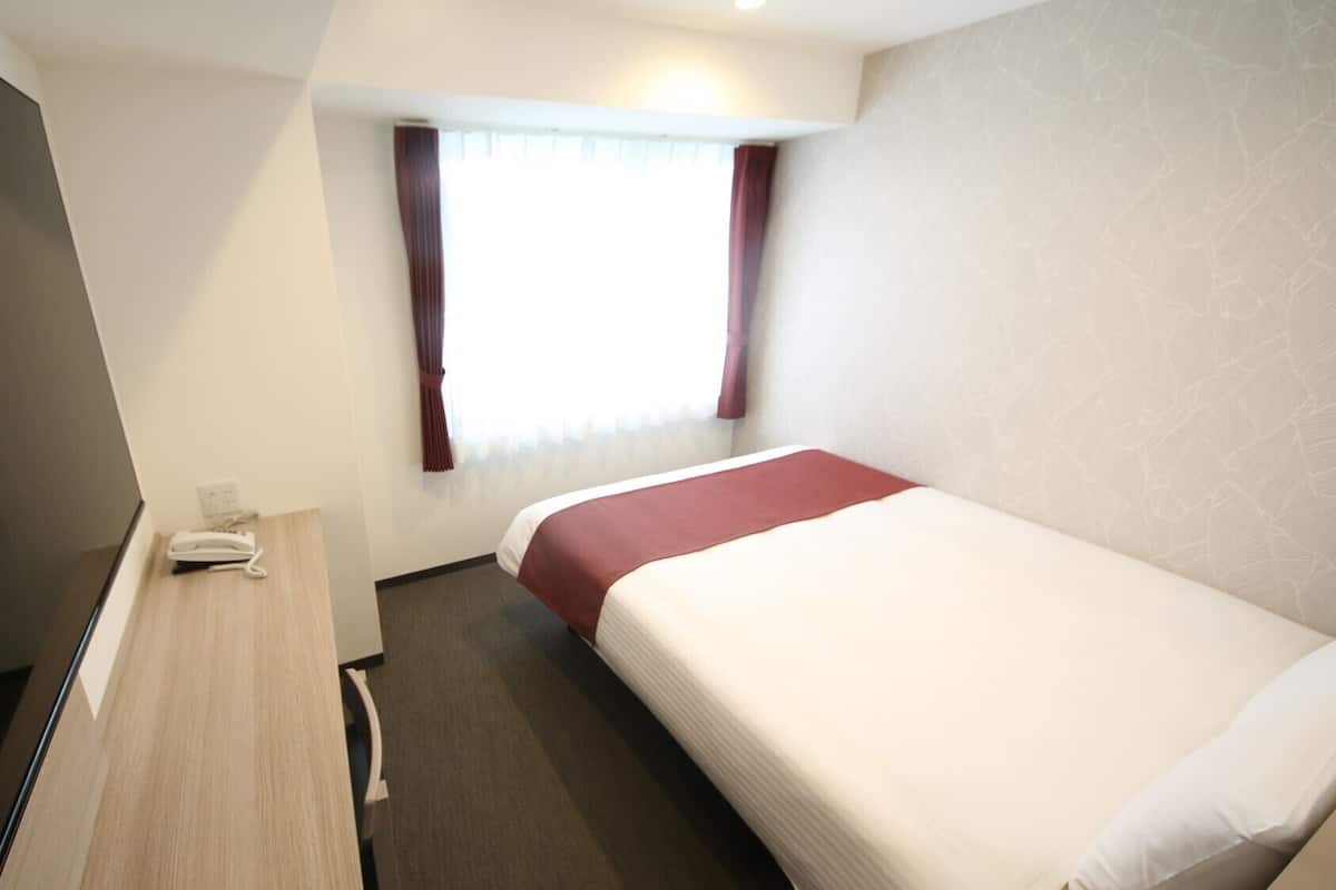 A hotel room with a bed, a desk, a telephone, and a window with curtains.