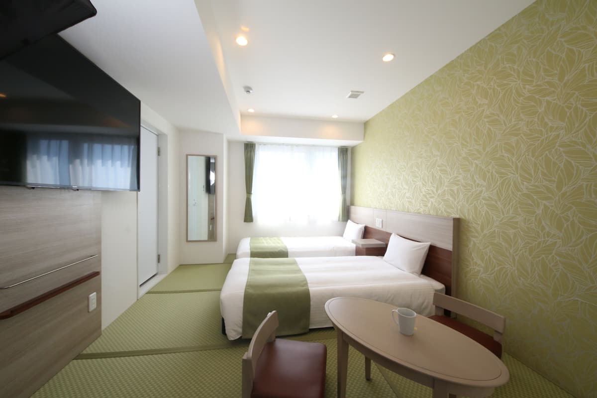 A hotel room with two beds, a dining table, a chair, a television, and a window with curtains.