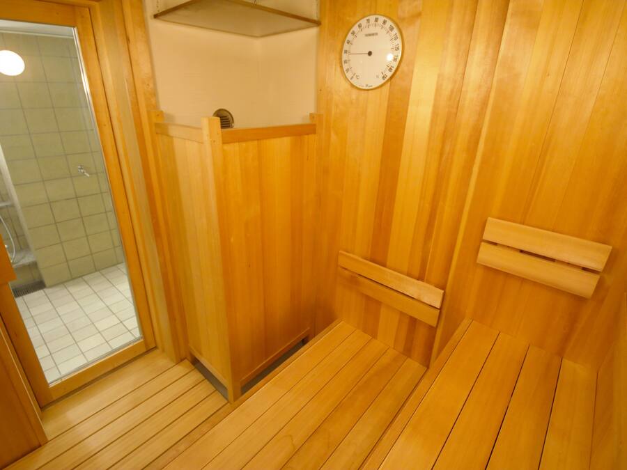 Un sauna de madera con un banco de madera, un termómetro en la pared y una puerta que da a un baño con azulejos.