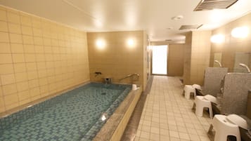 A bathroom with a tiled floor, a large bathtub, and a row of white plastic stools.