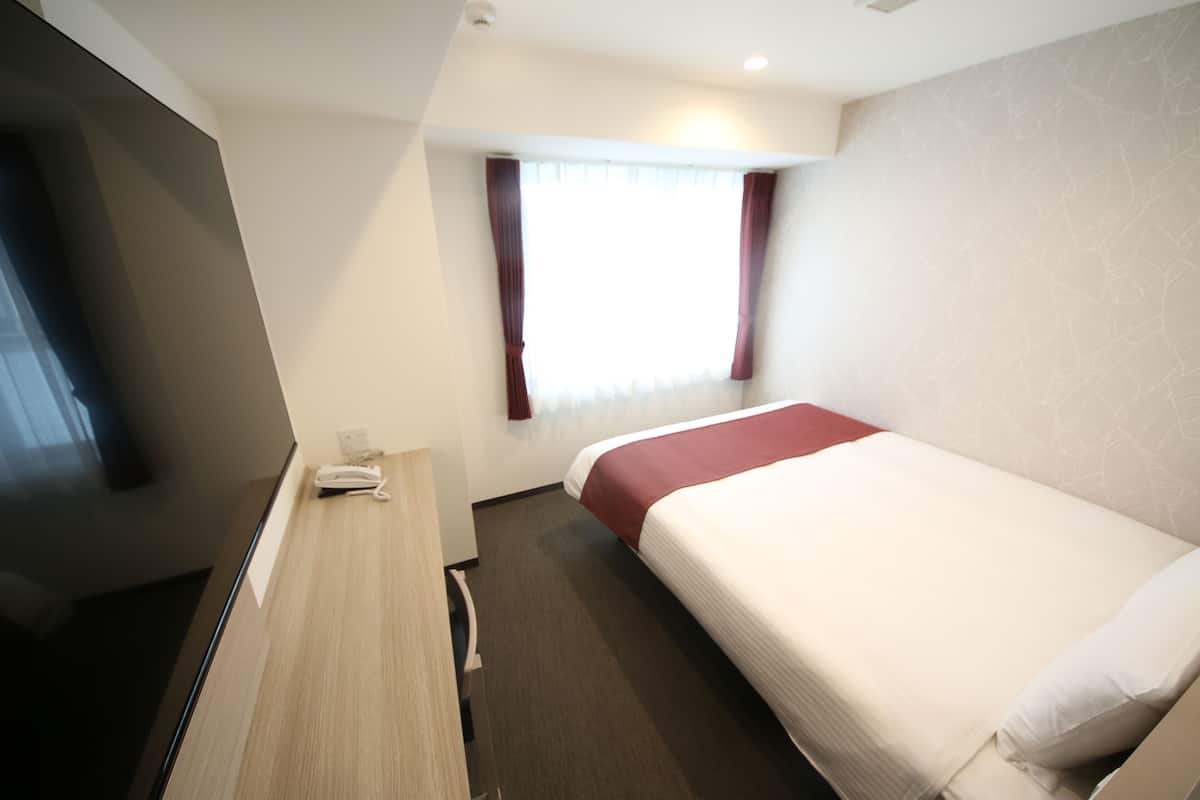 A hotel room with a single bed, a desk with a telephone, and a window with curtains.