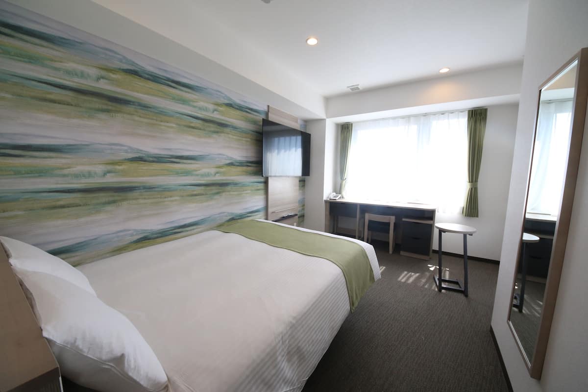 A hotel room with a large bed, a desk, a chair, a TV, and a large mirror.