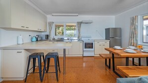 Eine moderne Küche mit weißen Schränken, einer zentralen Kochinsel mit Sitzgelegenheiten, einem Holztisch und Blick ins Grüne.