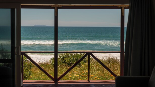 Ein Zimmer mit großem Fenster und Meerblick, einer Holzterrasse und Blick auf den Strand.