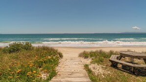 Ein hölzerner Steg führt zu einem Strand mit einem Picknicktisch.