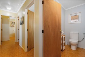 A hotel room with a wooden door, a white toilet, and a framed artwork on the wall. - Poppy's Beach House - Beachfront Whangapoua Home (Whangapoua)