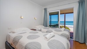 Ein Schlafzimmer mit zwei Betten, Blick auf den Strand und einer Schiebetür nach draußen.