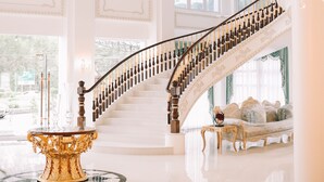 Una gran escalera con barandales ornamentales y un candelabro, que conduce a un balcón con vistas.