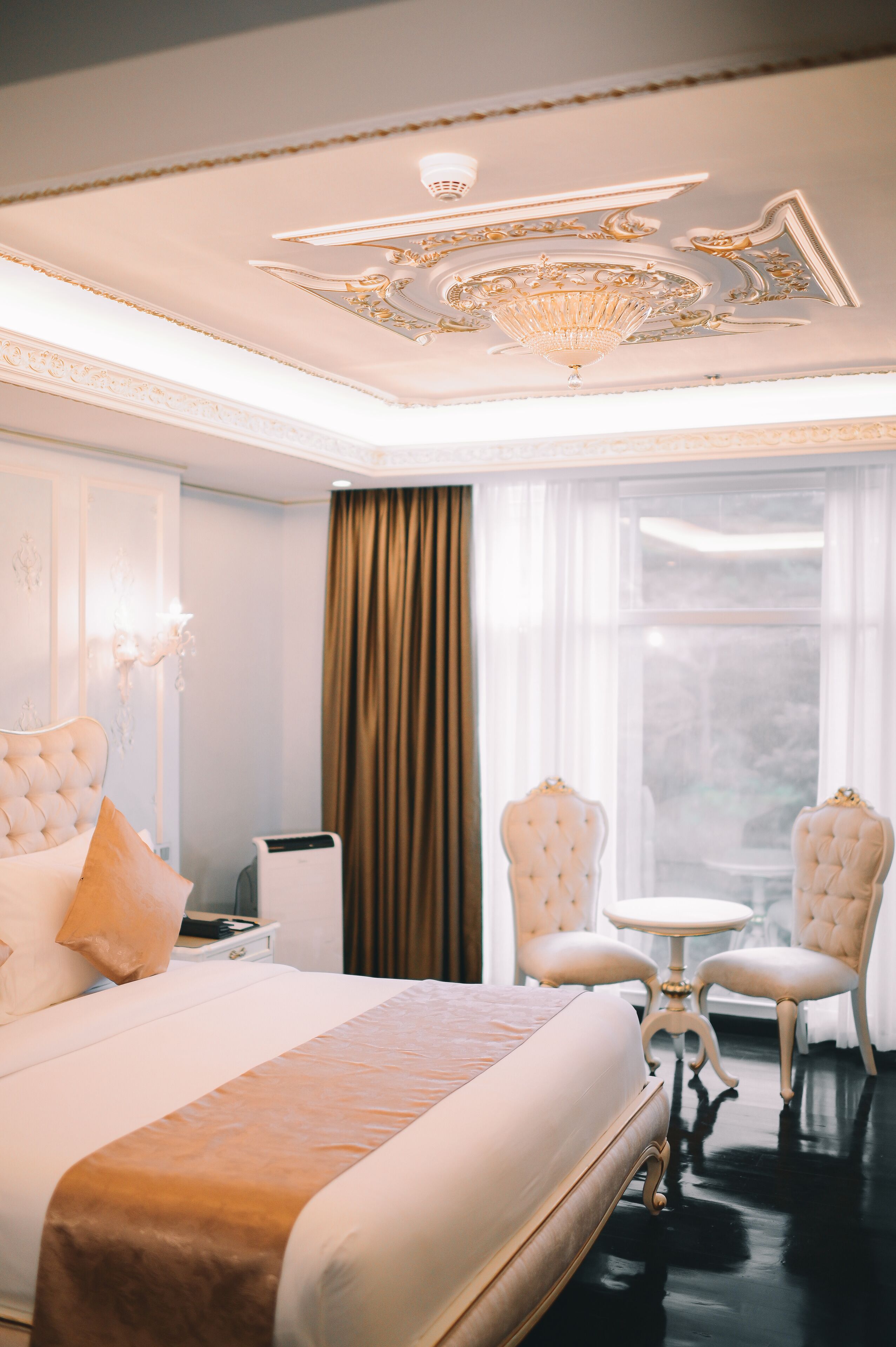 Una lujosa habitación de hotel con una cama grande, un candelabro, una mesa redonda y dos sillones.