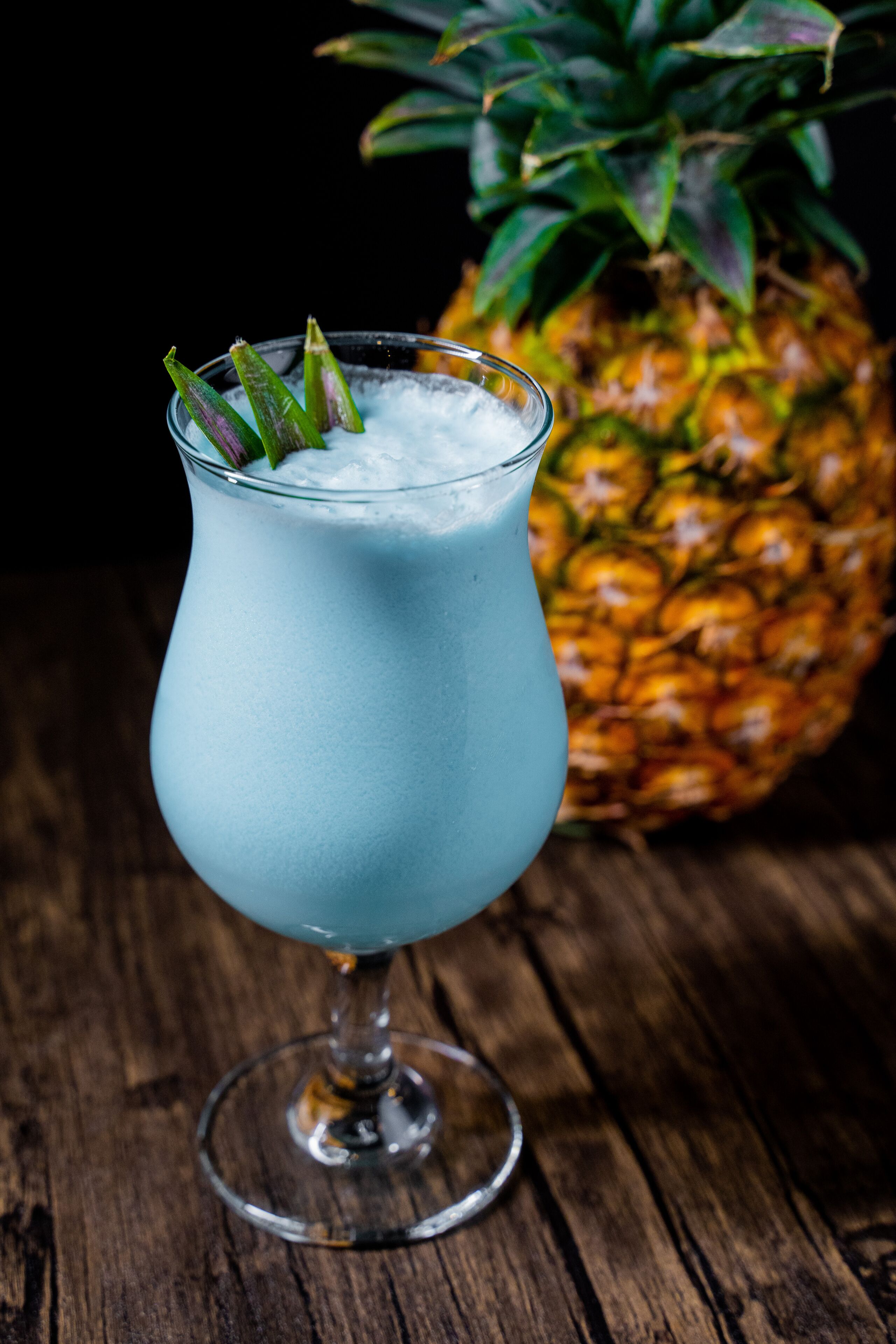 A glass with a blue beverage, garnished with green leaves, on a wooden surface.