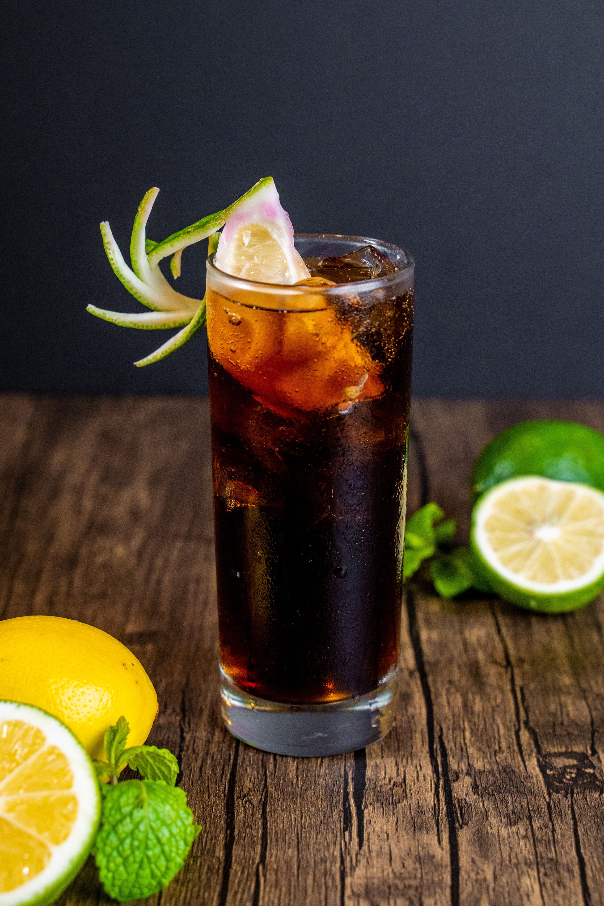 A tall glass of iced tea with a slice of lime and mint leaves, placed on a wooden surface with a dark background.