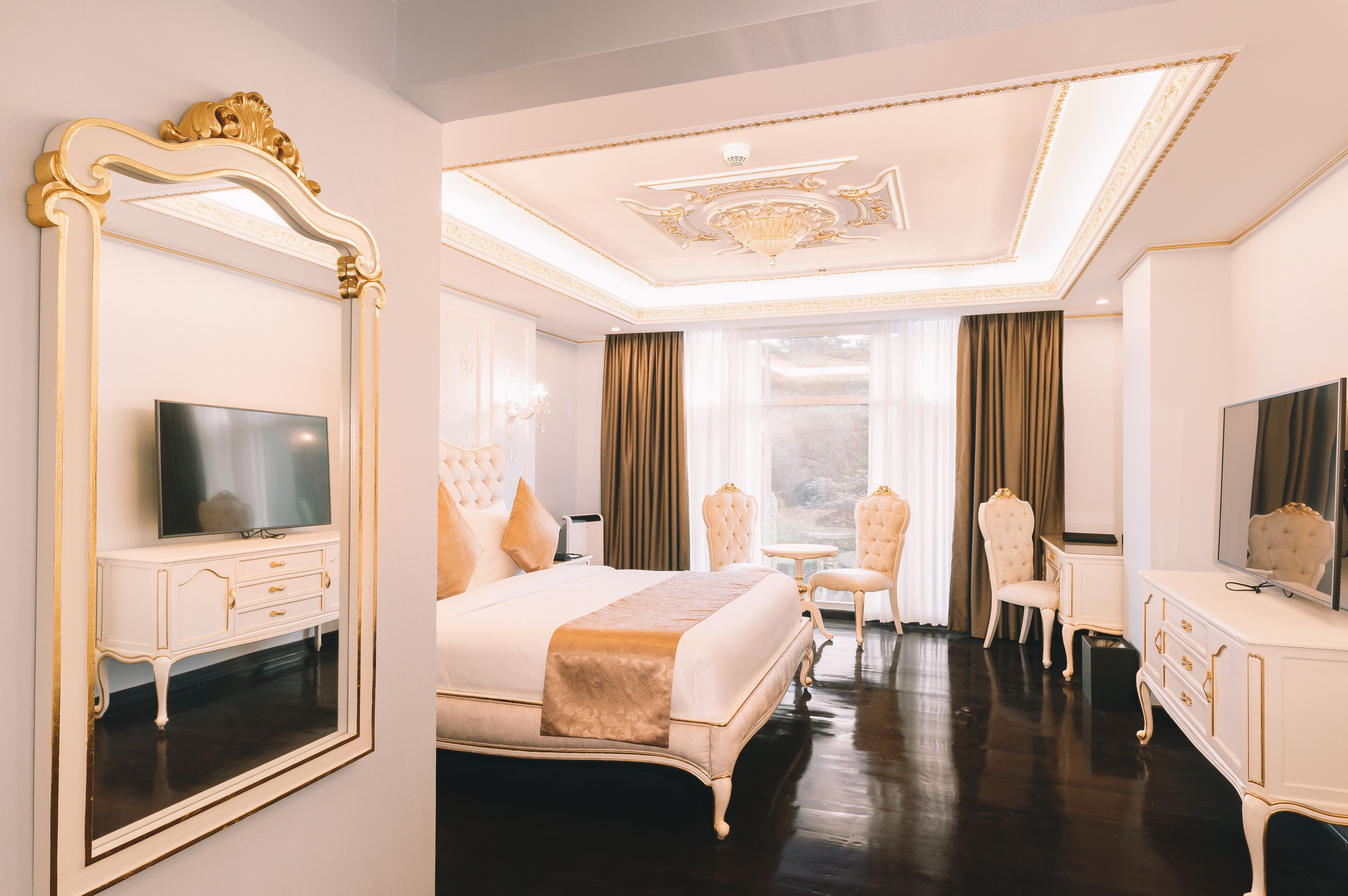 Una lujosa habitación de hotel con una cama grande, un rincón de descanso con una silla, un tocador con espejo y un televisor.