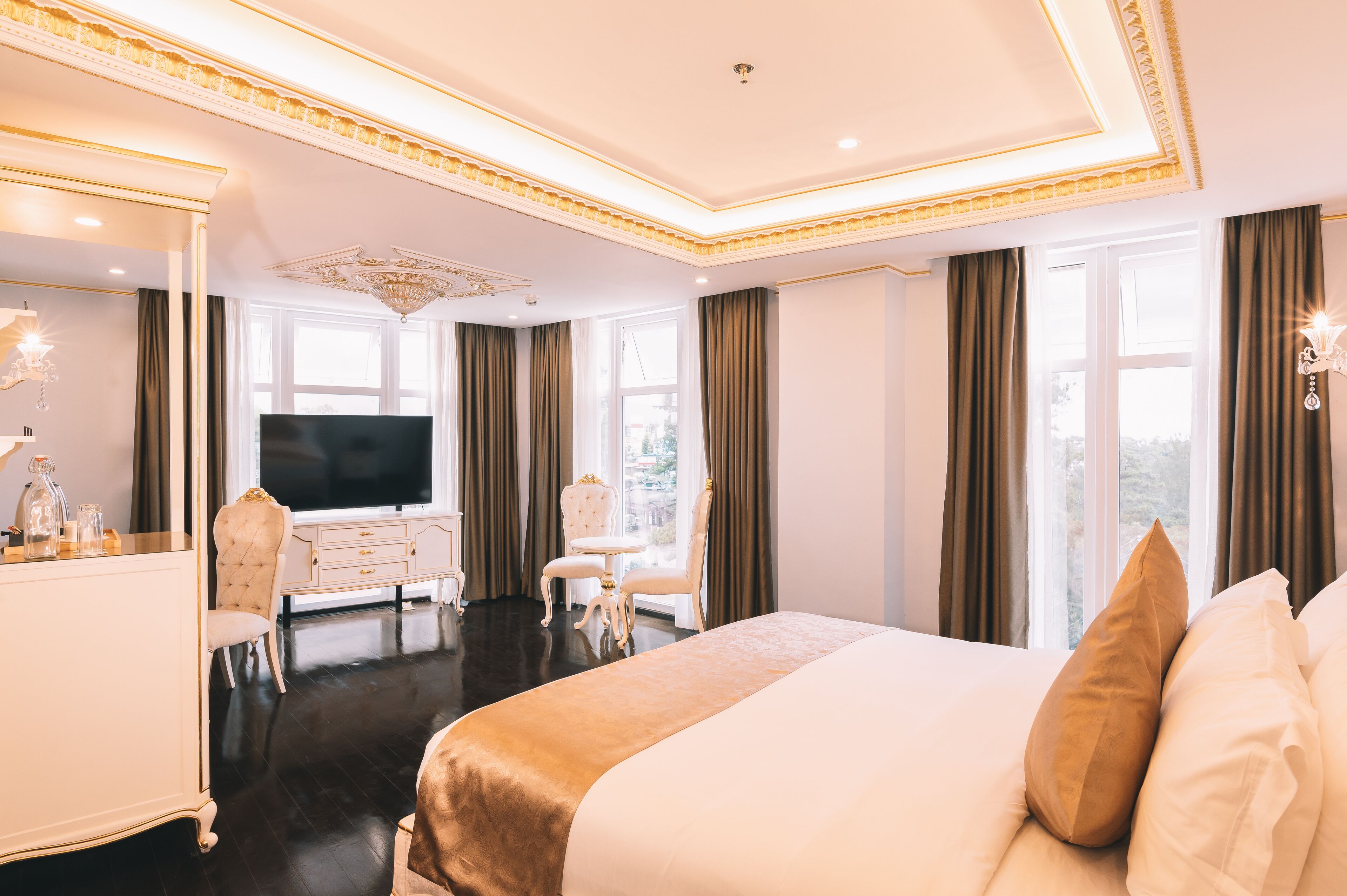 Une chambre d’hôtel luxueuse, dotée d’un grand lit, d’une télévision, d’une coiffeuse avec un miroir et d’un lustre.