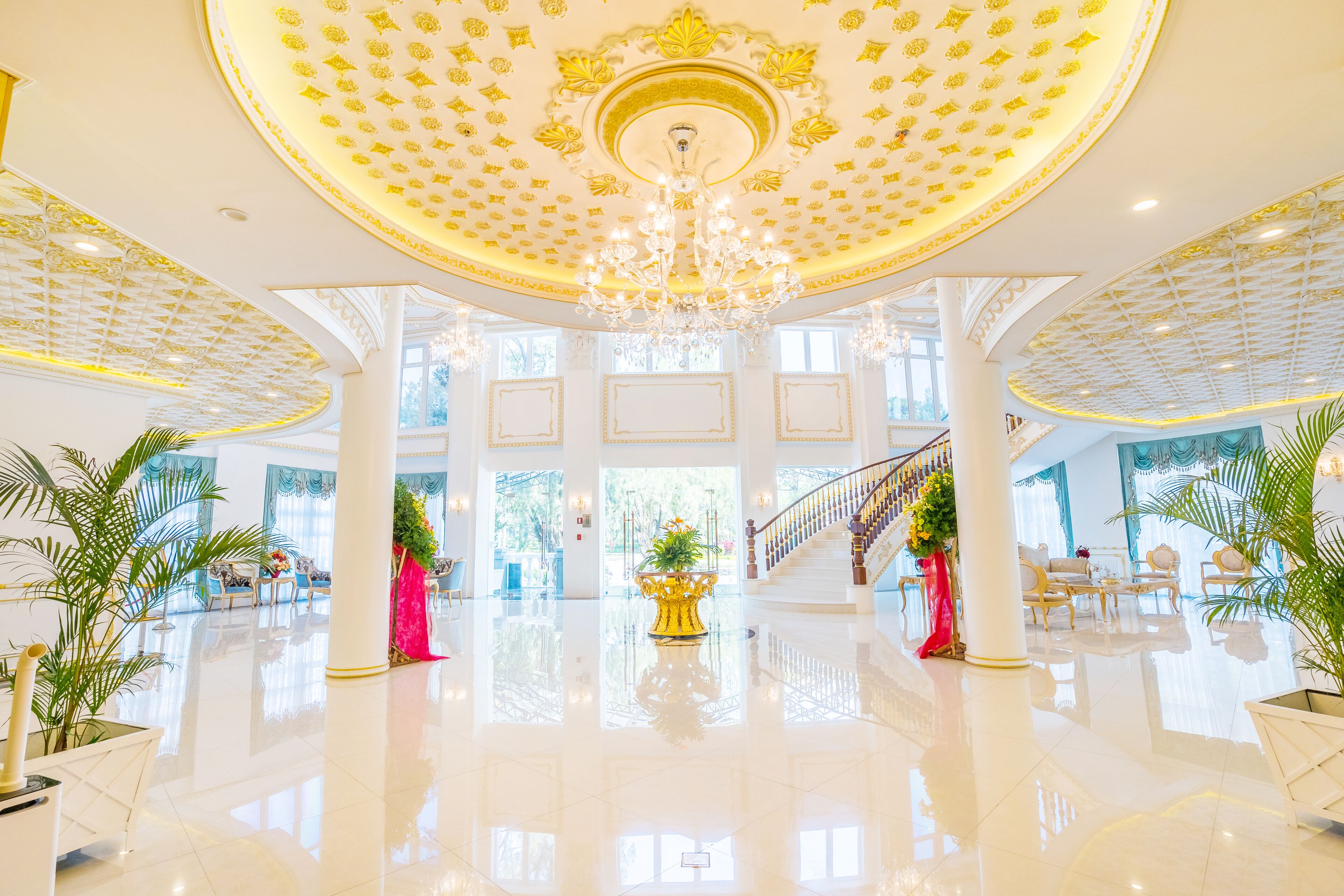 A spacious lobby with a high ceiling, chandeliers, and a central staircase.