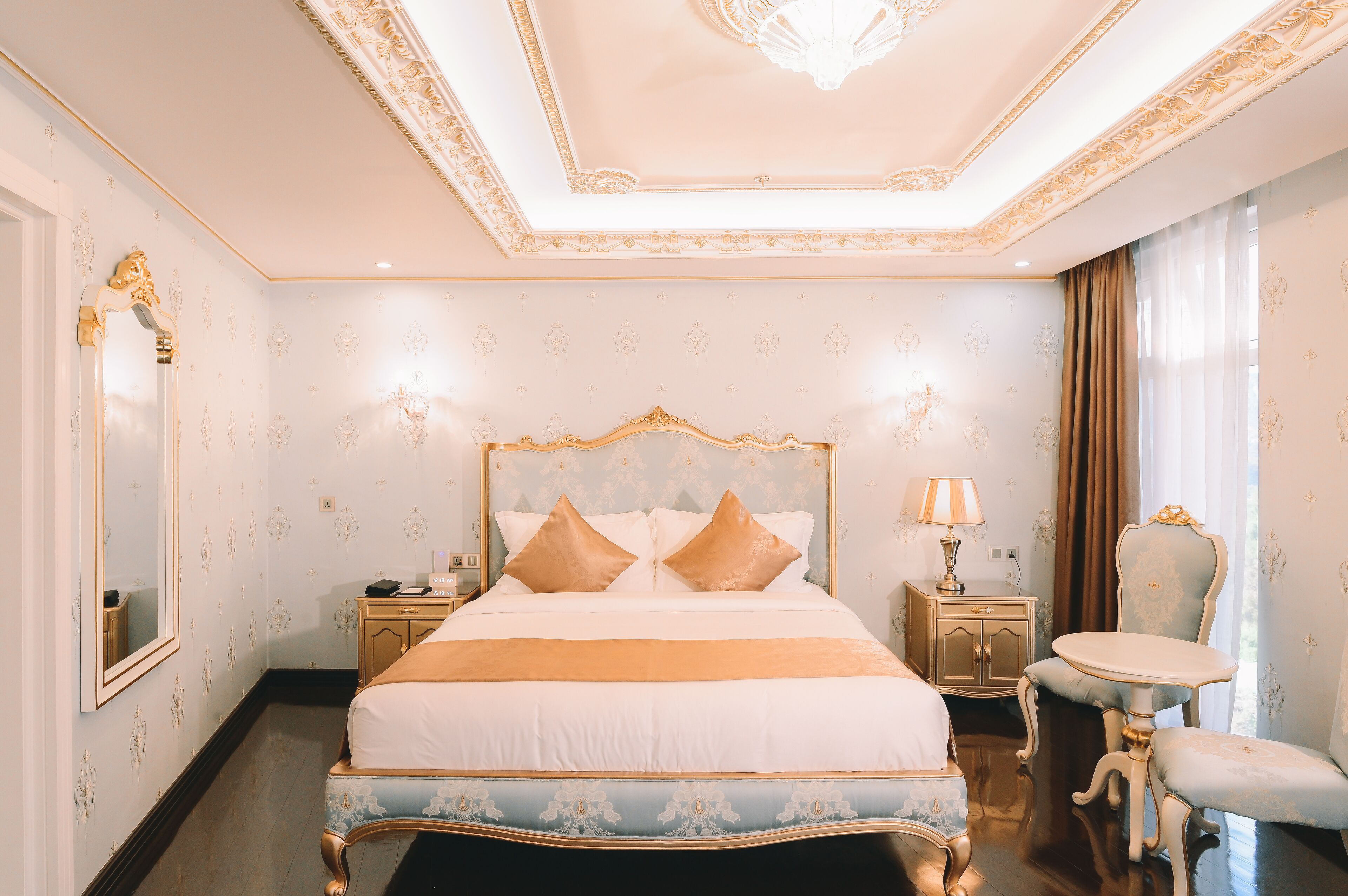 Een slaapkamer met een groot bed, een nachtkastje, een lamp, een stoel en een spiegel.