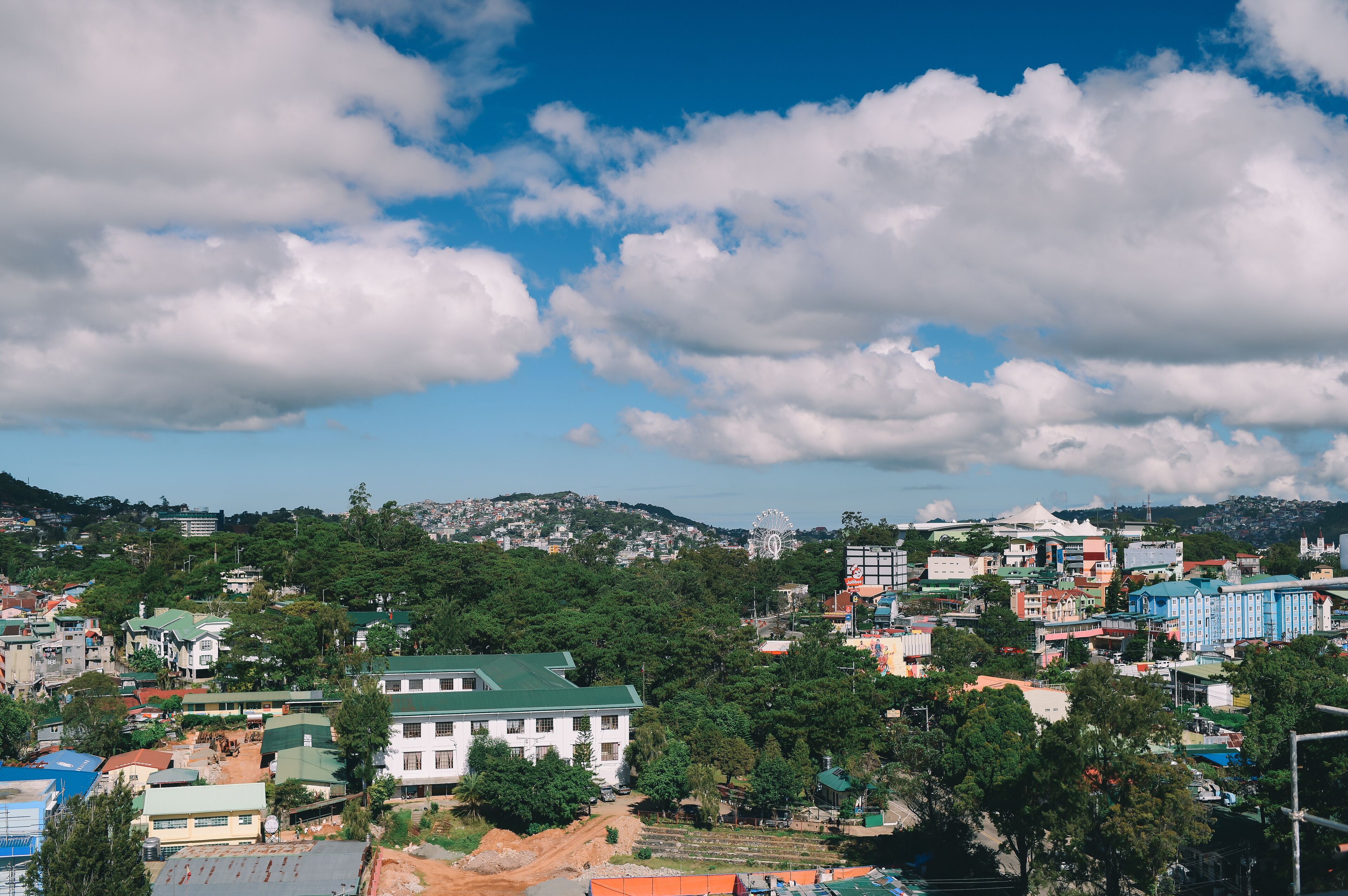 A cityscape with a prominent white building with a green roof, surrounded by dense greenery and other buildings.