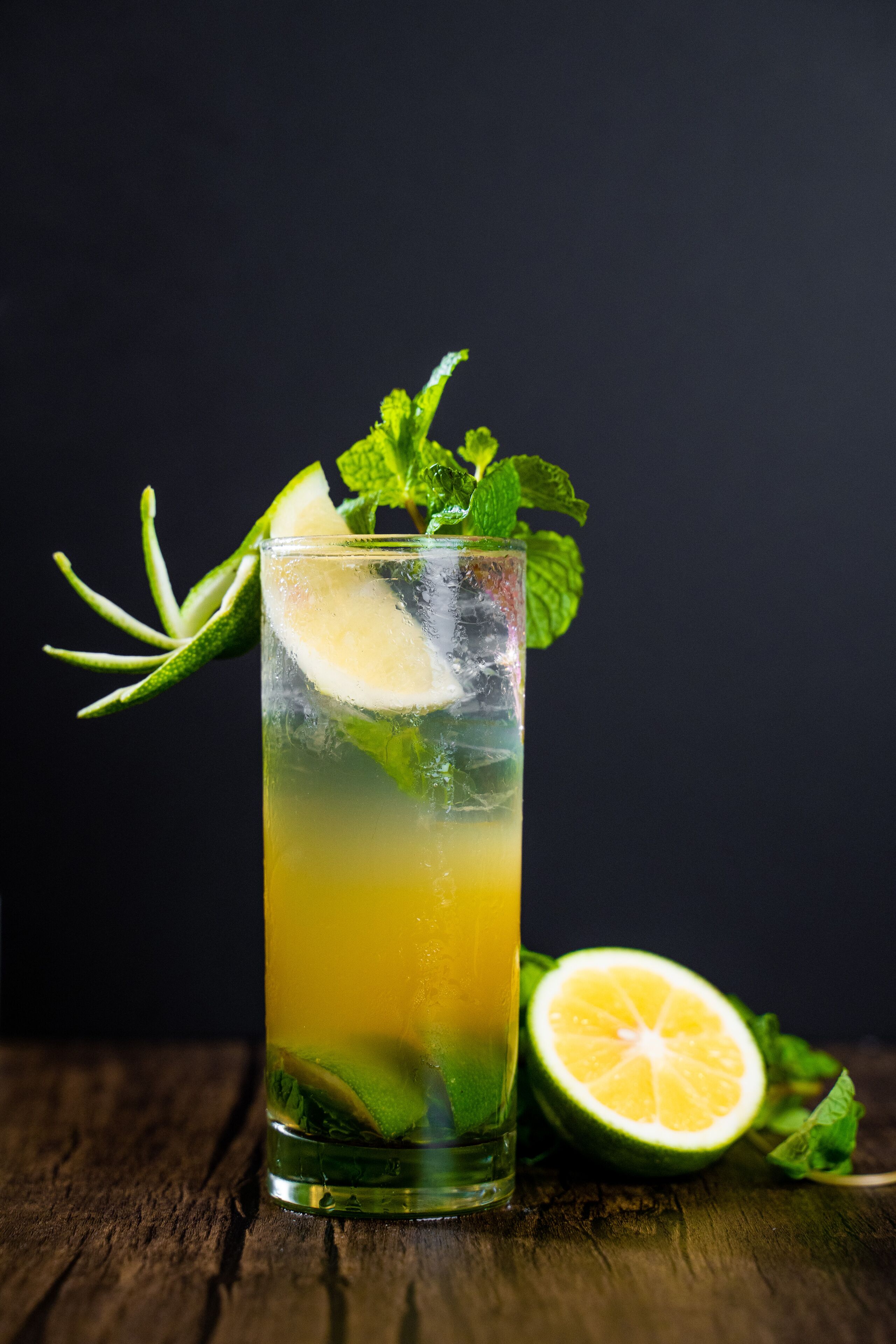 A tall glass with a layered drink, garnished with mint and lime, on a wooden surface.