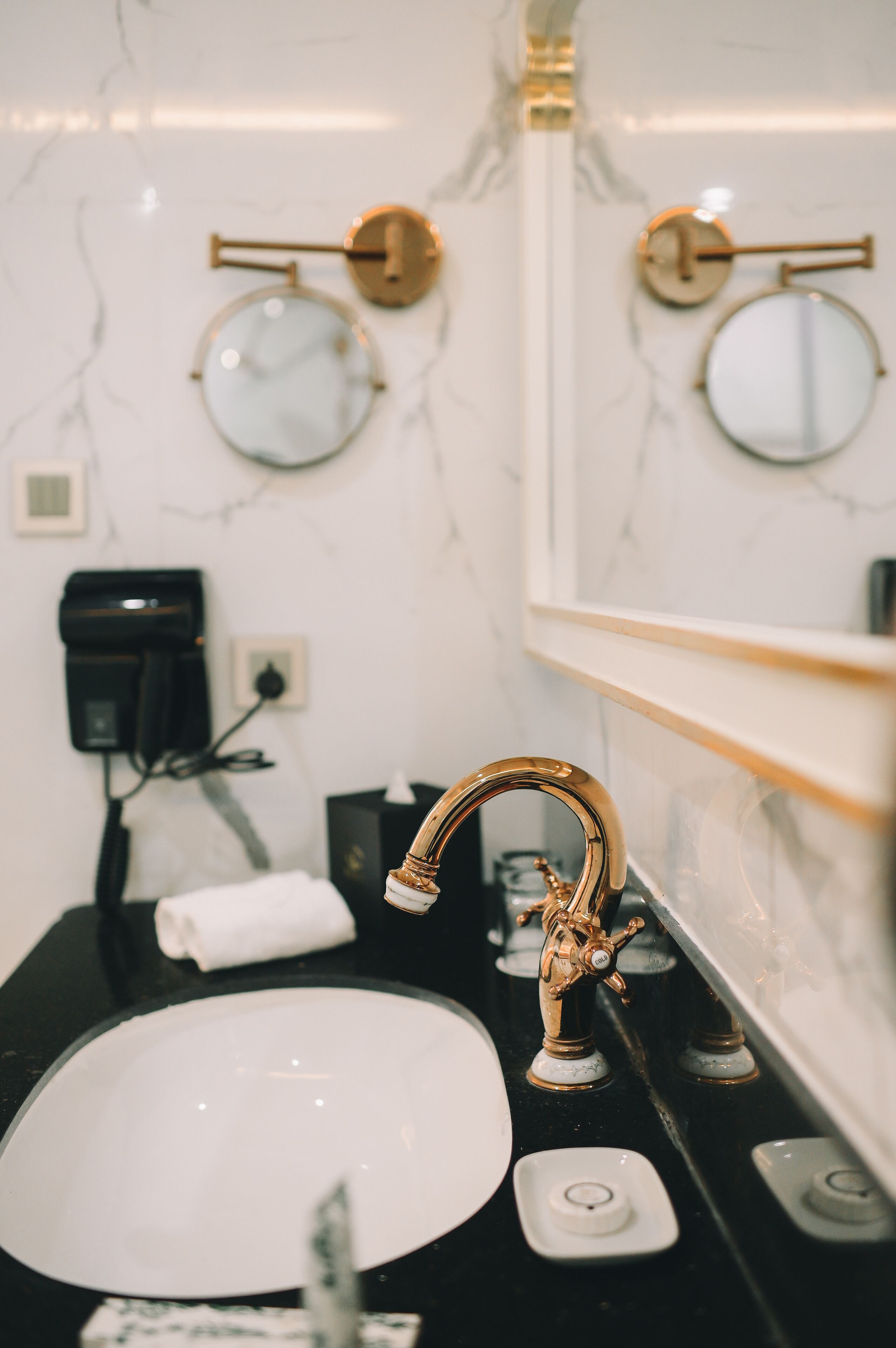 A bathroom with a gold faucet, a white sink, and two round mirrors on the wall.