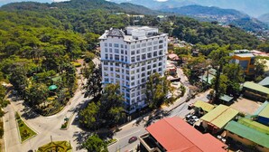 Un hotel de varios pisos con diseño moderno, rodeado de exuberante vegetación y montañas al fondo.