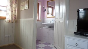 Una habitación pequeña y funcional con piso a cuadros, un lavamanos blanco, un espejo y un televisor sobre una cómoda.
