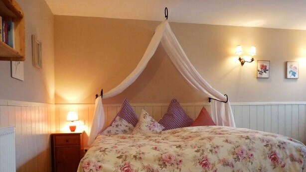Un dormitorio con cama a dosel, una mesita de noche con lámpara y apliques de pared.