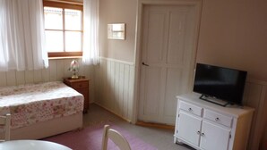 Un dormitorio con cama, cómoda, televisor, ventana con cortinas y puerta.