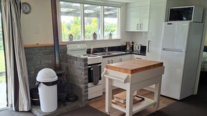 Een compacte keuken met een fornuis, spoelbak en koelkast. Er is een raam met uitzicht op groen.