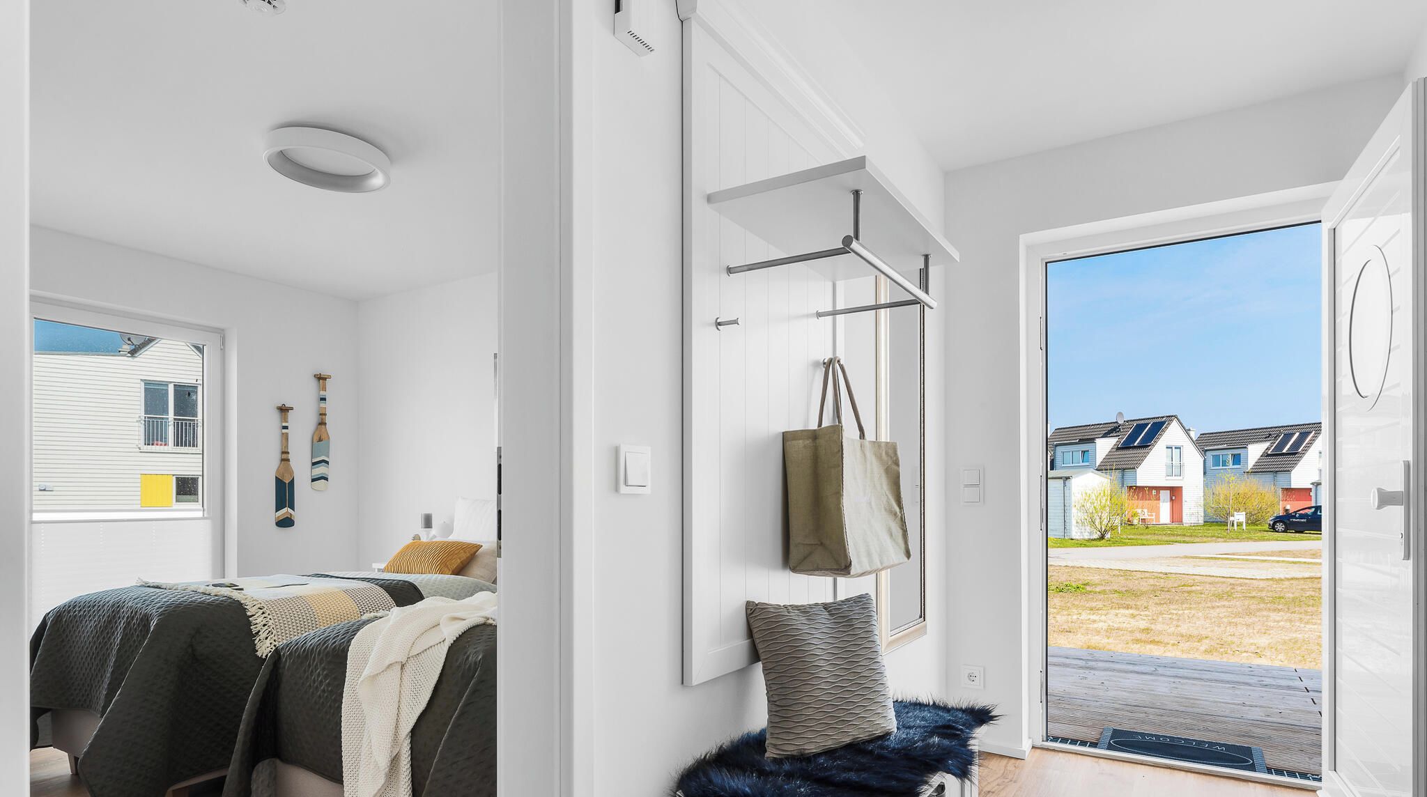 A modern bedroom with a bed, a hanging bag, and a view of a residential area through an open door.