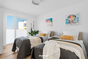 A modern bedroom with two beds, a large window, and artwork on the walls.