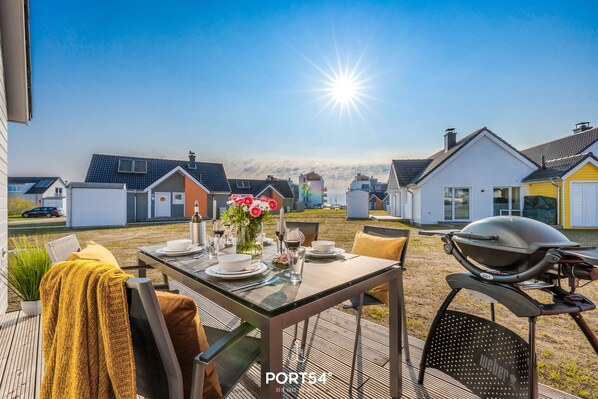 A patio with a table set for dining, a grill, and a view of a residential area.