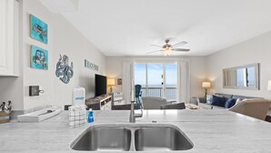 A modern kitchen with a double sink, a ceiling fan, and a view of the ocean through large windows. - Renovated 1BR Celadon Condo | Gulf Views, Balcony, Bunks + Beach Chairs Included! (Panama City Beach)