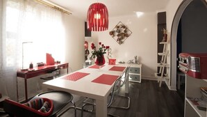 A dining area with a white table, red placemats, and a red pendant light. There is a vase with flowers on the table, and a red car model on the right. - entre parc et Haras - Hennebont (Hennebont)