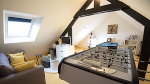 A cozy loft-style room with a foosball table, a comfortable sofa, a small desk with a computer, and a window providing natural light. - entre parc et Haras - Hennebont (Hennebont)