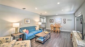 A living room with a blue sofa, a coffee table, and a dining area with a wooden table and chairs. - Near Beaches and Speedway! Dog-Friendly Hidden Gem (Port Orange)
