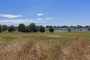 Un campo de golf con un estanque, árboles y cielo despejado.
