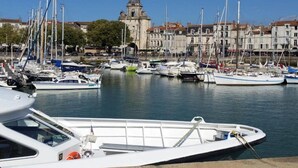 A marina with multiple boats docked, a prominent clock tower in the background, and buildings lining the waterfront. - Luxury Villa in France with Private Pool (Les Forges)