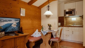 Un intérieur en bois comprenant une télévision, un banc en bois, une table avec un vase et un coin cuisine équipé d’un four à micro-ondes.