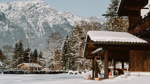Een houten lodge met een sneeuwbedekte dak, omringd door besneeuwde bomen en bergen.