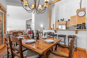 A dining area with a wooden table set for four, surrounded by chairs. A chandelier hangs above, and a clock is mounted on the wall. - RMR: Moose Creek 17 Townhome in Teton Village (Teton Village)