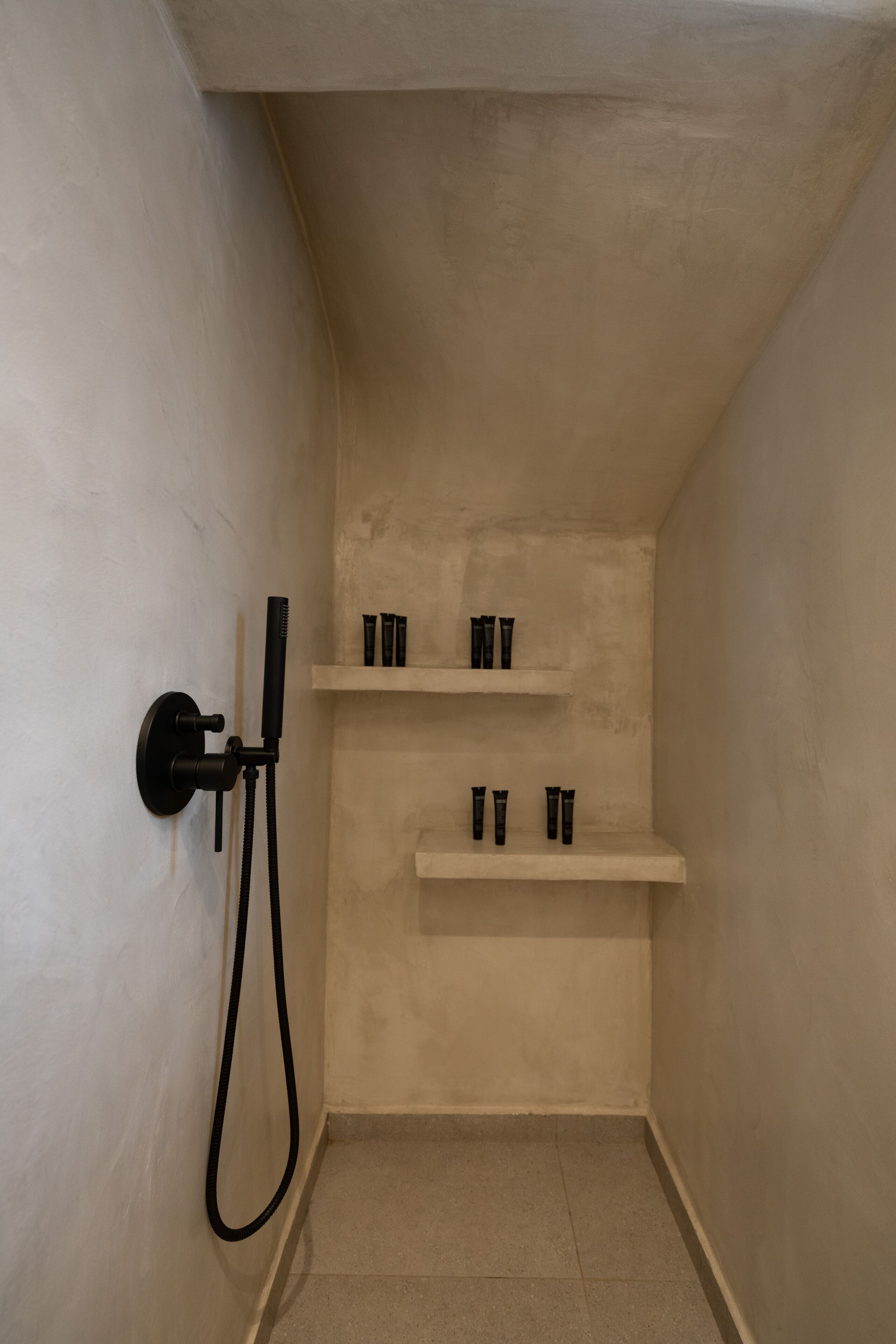 A small, enclosed bathroom with a shower, two shelves with toiletries, and a towel rack.