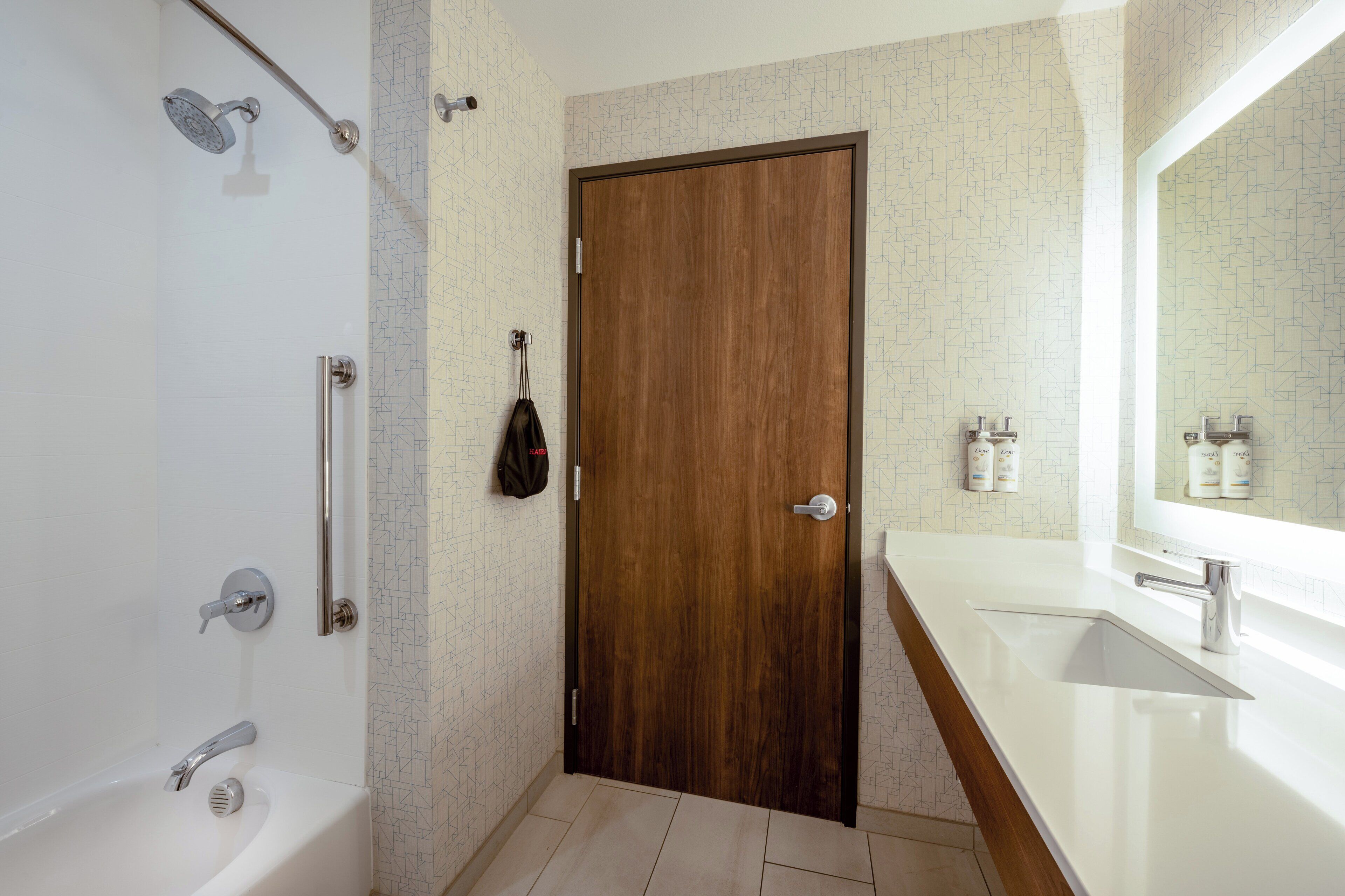 Un baño moderno con puerta de madera, un lavabo blanco y una ducha con cabezal de ducha manual.