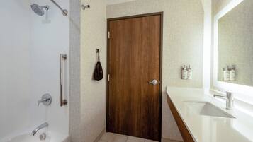 Un baño moderno con puerta de madera, un lavabo blanco y una ducha con cabezal de ducha manual.