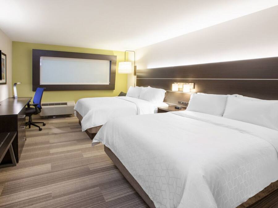 Habitación de hotel con dos camas, un escritorio, una silla, un televisor y una pantalla para proyector.